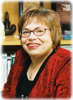 Judith (Judy) Heumann - smiling and wearing a red shirt and glasses